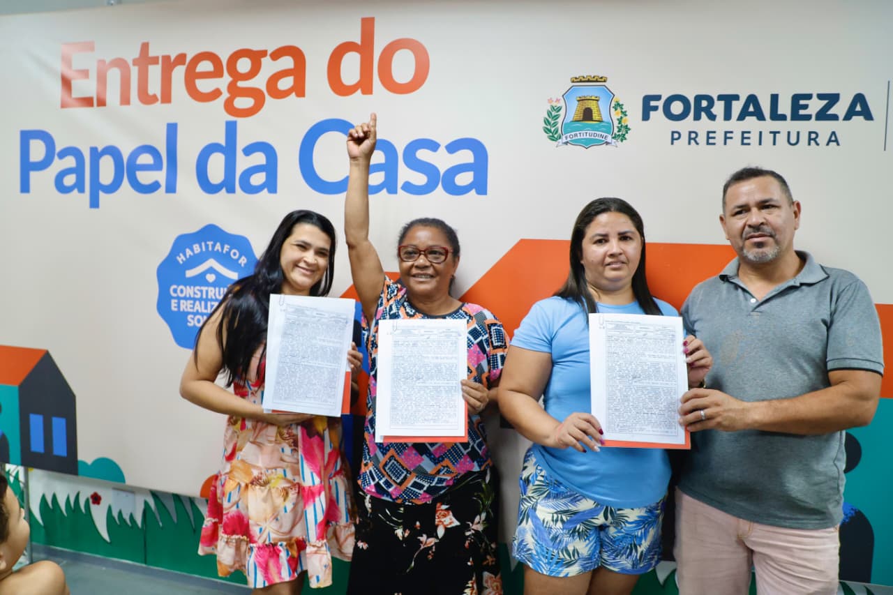 grupo de pessoas posa para a foto segurando os documentos recebidos de regularização fundiária